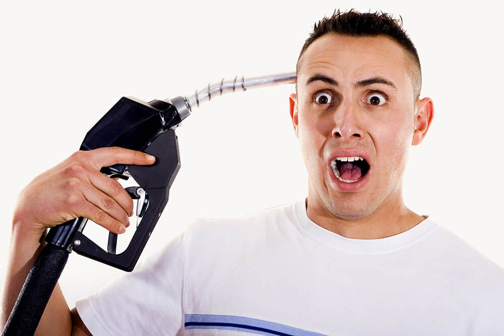 Man holds petrol pump to his head as a gun symbolising the increase in petrol price and the effect it has on consumers