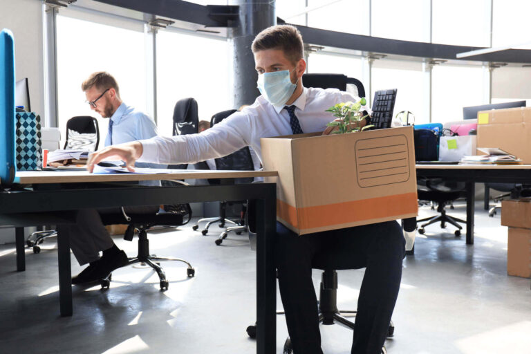 Man packing up office belongings while wearing a mask facing unemployment during Corona lockdown
