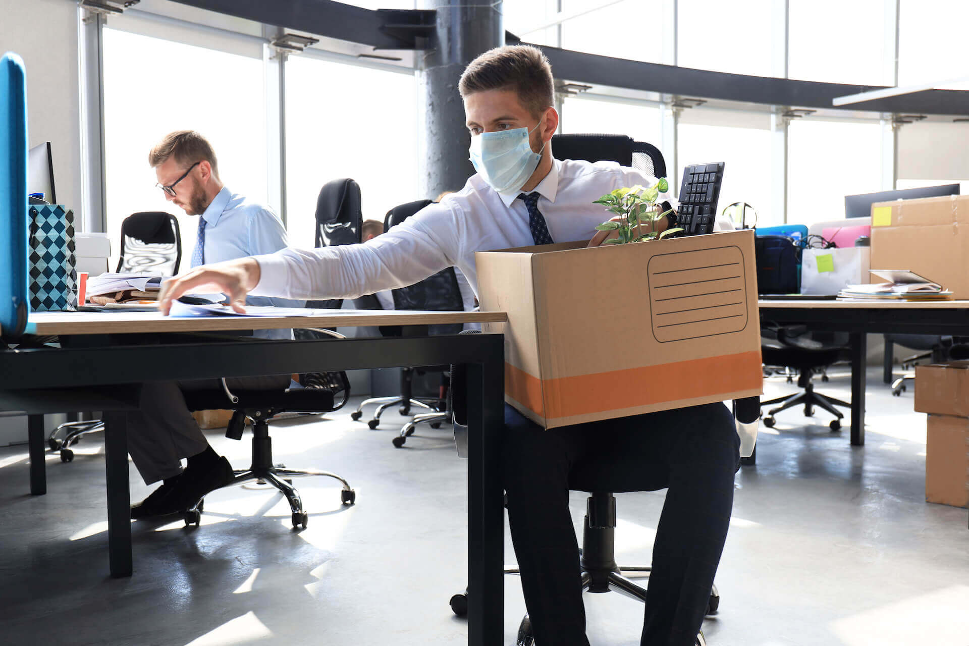 Man packing up office belongings while wearing a mask facing unemployment during Corona lockdown