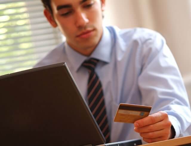 Man looking at credit card sitting behind his computer contemplating buying on credit again.